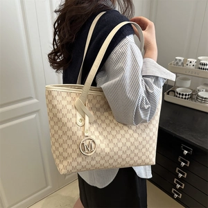 Retro cream tote bag with brown M-pattern and metallic charm shown on model shoulder