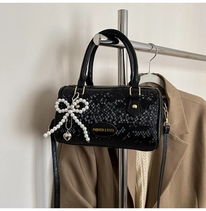 Détail du sac noir à motif serpent avec nœud en perles et breloque en forme de cœur