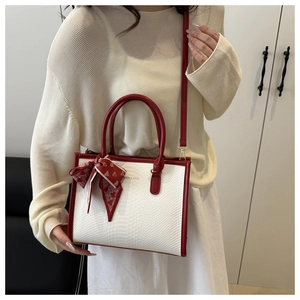 Detail of white crocodile texture tote with red handles and decorative silk scarf