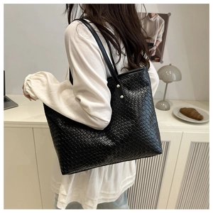 Detail of a black woven leather tote bag shown on a model in a minimalist stylish room