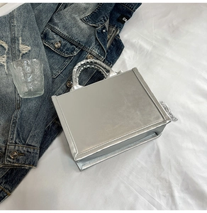 Silver metallic handbag with silk scarf detail displayed on white fabric next to denim