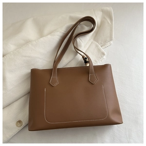 Detalle de bolso tote marrón con costuras en U y un pañuelo de seda decorativo en el asa