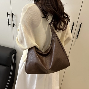 Large brown Maillard-style leather tote bag shown on model in minimalist indoor setting