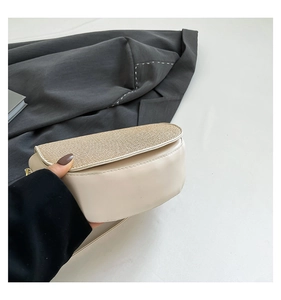 Detail of beige saddle bag featuring gold woven flap and smooth leather texture