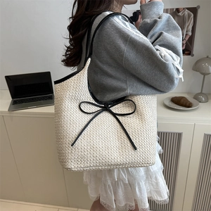 Minimalist cream woven tote bag with black bow detail and straps in a casual lifestyle setting
