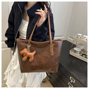 Detail of a brown tote bag with stitching texture and a cute puppy charm shown on a model