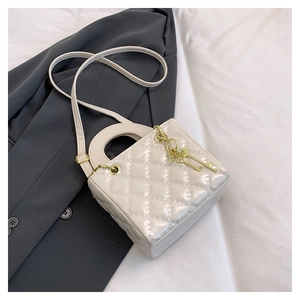 Dettaglio mini borsa trapuntata bianco crema con trama lucida e ciondolo a chiave dorata