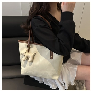 Detail of quilted cream tote bag with contrast brown straps and dog charm