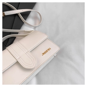 Detail einer cremeweißen Lederschultertasche mit goldenem JINGPIN Logo und Klappendesign
