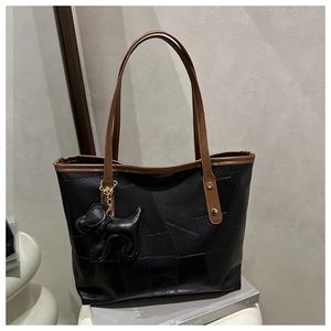 Detail of black leather tote bag with geometric stitching, brown strap, and dog charm