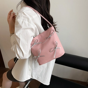 Pink shoulder bag with silver bow details shown on a model for casual style