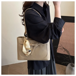 Détail du sac bandoulière en cuir kaki avec foulard en soie sur la poignée porté par mannequin