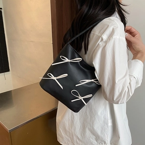 Elegant black shoulder bag with cream bows shown on model for a trendy spring look