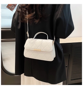 Detail of white quilted crossbody bag with gold hardware worn on black blazer