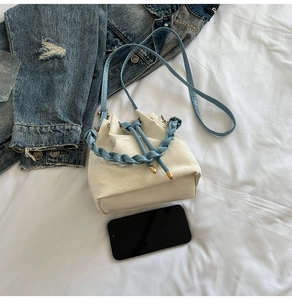 Detail of cream drawstring bucket bag with blue woven handle and gold hardware accents