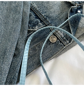 Detail view of dark wash denim bag with a vintage silver metal button and light blue strap