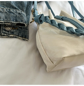 Detail of white glossy mini bucket bag featuring blue braided handle and contrast stitching