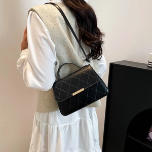 Elegant black quilted crossbody bag with gold buckle shown on a model in a modern interior