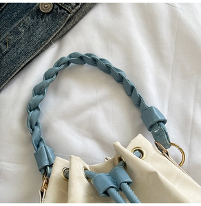 Close-up of cream white bucket bag featuring blue braided leather handle and gold eyelets