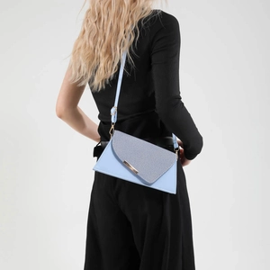 Sac bandoulière bleu clair texture denim et détails dorés porté par un mannequin