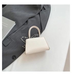 Détail d'un sac à main trapèze beige avec chaîne argentée sur blazer gris et livre