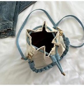 Top view of cream bucket bag with blue braided handle and gold-tone drawstring hardware