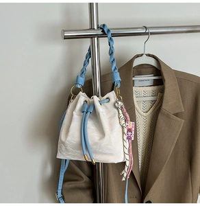 Detail of cream drawstring bucket bag with blue woven handle and decorative charm