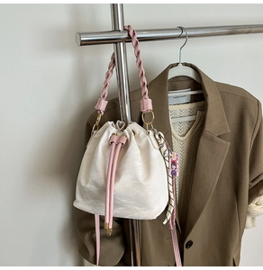 Detail of white drawstring bucket bag with pink braided handle and silk scarf charm