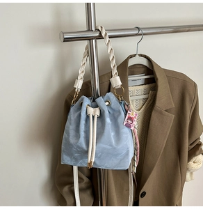 Detail of light blue bucket bag with woven handle, drawstring closure and pink charm