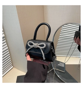 Détail d'un mini sac en cuir noir avec un nœud en strass argentés et bandoulière chaîne