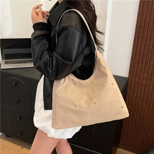 Sac hobo beige chic avec clous dorés porté par un mannequin en tenue décontractée