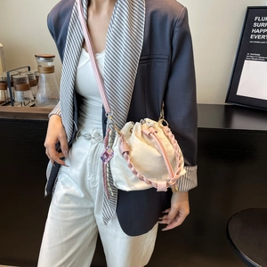 White leather drawstring bucket bag with pink woven handle and long shoulder strap