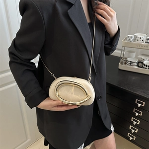 Elegante borsa a tracolla crema con manico dorato e catena su giacca nera sartoriale