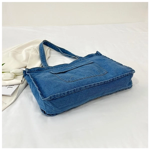 Detail view of a blue denim tote bag with front flap pocket on white fabric background