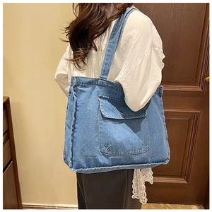 Detail of blue denim tote bag showing the front flap pocket and textured washed fabric