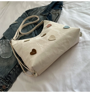 Detail of cream tote bag featuring textured leather and colorful heart-shaped patches