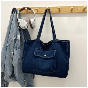Detail of dark blue denim tote bag with front flap pocket and metal buckle detail