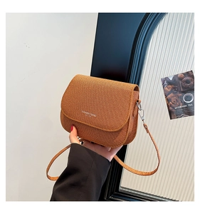 Close-up of brown woven texture saddle bag with fashion trend lettering and slim strap