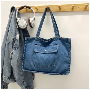 Detailed close-up of a blue denim tote bag with a front flap pocket and metal button