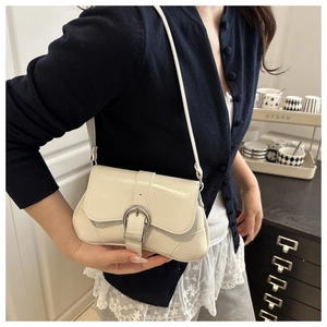 Detail of a creamy white glossy underarm bag with a silver horseshoe buckle and strap