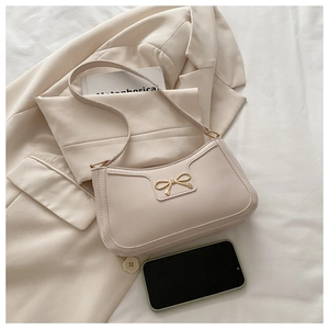 Close-up of cream shoulder bag with golden bow buckle on a beige suit jacket
