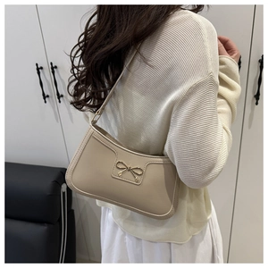 Detail of a beige bow handbag showing the smooth matte leather texture and gold bow buckle