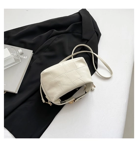 Close-up of off-white lychee leather shoulder bag with geometric stitching and gold buckle