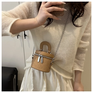 On-body shot of a woven cylinder bag with leather top handle and metal chain strap