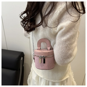 Detailed view of a pink mini cylinder bag with woven texture and chain strap worn by model