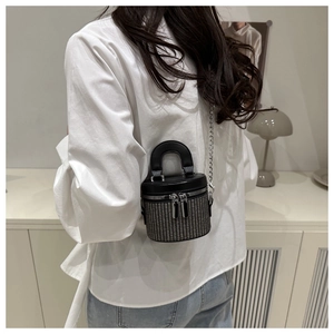 Detail of a mini woven cylindrical bucket bag with black leather flap and chain strap