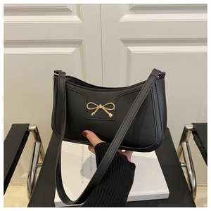 Detail of a black leather underarm bag featuring a golden bow buckle and adjustable strap