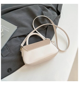 Detail of cream crossbody bag with textured flap and gold hardware on grey suit