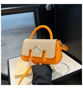 Detail of orange handbag with beige woven texture flap and golden circular metal buckle