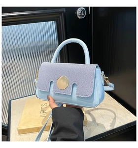 Detail of light blue denim textured handbag with gold circular clasp and leather handle